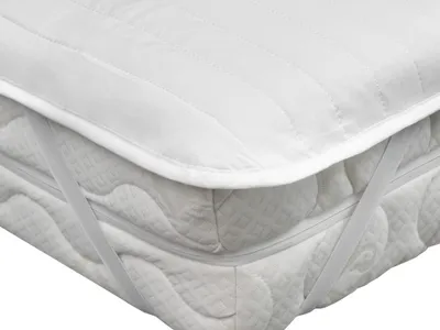 A close-up view of a white quilted mattress protector with elastic straps on a mattress.