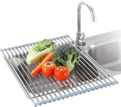 A roll-up dish drying rack with various vegetables placed on it, positioned over a kitchen sink with a faucet.