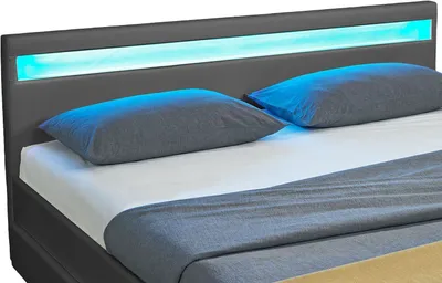 A close-up view of a bed with a gray headboard featuring blue and cyan LED lighting, and two gray pillows.