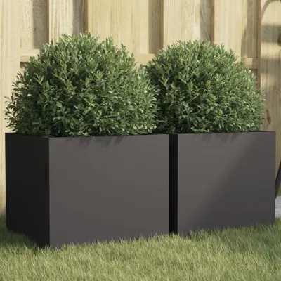 Two black square planters with green bushes in them, placed on grass in front of a wooden fence.
