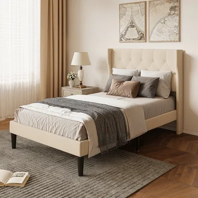 A bedroom scene featuring a bed with pillows and a blanket, a bedside table with a lamp, and artwork on the wall.