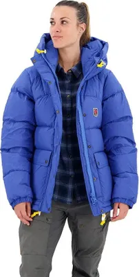 A woman wearing a blue puffer jacket and gray pants, posing for a product shot.
