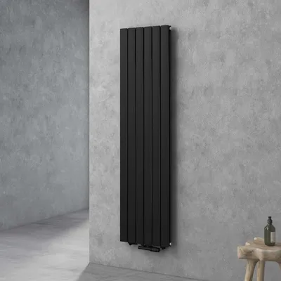 A tall, black, vertical radiator is mounted on a textured gray concrete wall in a modern bathroom setting. A small wooden stool with a bottle on it is visible to the right.