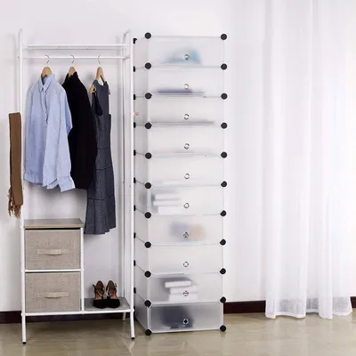 A white modular shoe rack with 10 transparent compartments is shown next to a white clothing rack with clothes and a scarf. Two fabric storage drawers are on the bottom shelf of the clothing rack, and a pair of brown high heels are on the floor.