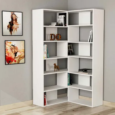 A white corner bookshelf filled with books and decorative items, placed against a light gray wall with two framed paintings.