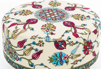 A close-up view of a round ottoman with a cream-colored fabric featuring a colorful floral and geometric pattern.