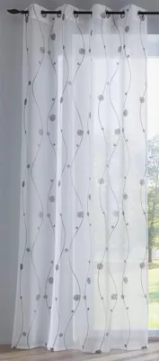 A white sheer curtain with a silver embroidered pattern of wavy lines and circles hangs in front of a window.