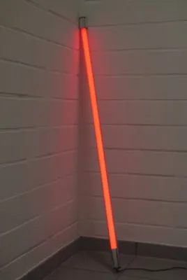 A red neon tube light stands in the corner of a room, leaning against the wall.