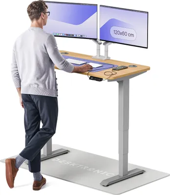 A man is standing at a height-adjustable desk with two monitors.