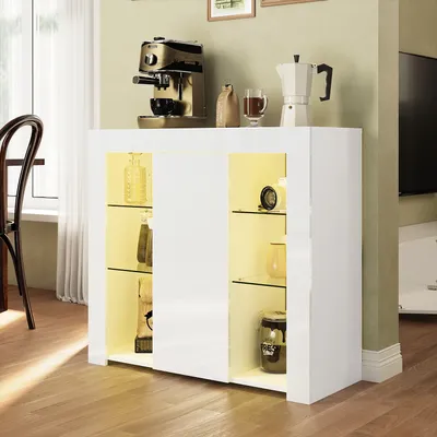 A white high-gloss sideboard with glass shelves and LED lighting, displaying decorative items and kitchen appliances on top.