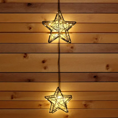 Two star-shaped string lights hang vertically against a wooden plank wall.