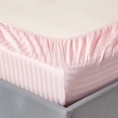 A close-up view of a pink striped fitted sheet on a bed.