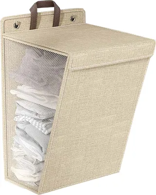A beige fabric laundry basket with a mesh front, filled with folded clothes, is mounted on a wall.