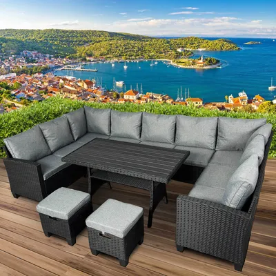 An outdoor seating set with a table and stools is placed on a wooden deck with a scenic view of a coastal town and bay in the background.