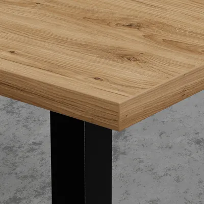 A close-up view of a table's corner, showing the wood grain of the tabletop and a black metal leg.