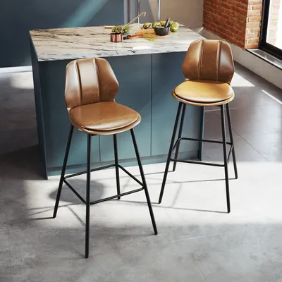 Two brown bar stools with backrests are placed in a modern kitchen setting, next to a kitchen island with a marble countertop. The lighting creates shadows on the floor.