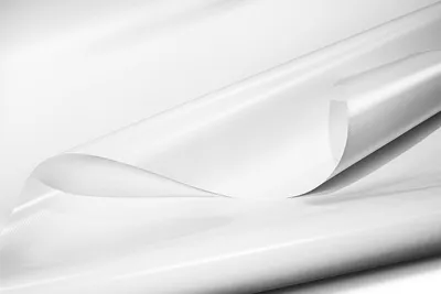 A close-up, studio shot of a white PVC tarpaulin material, with one edge curled to reveal the underside.