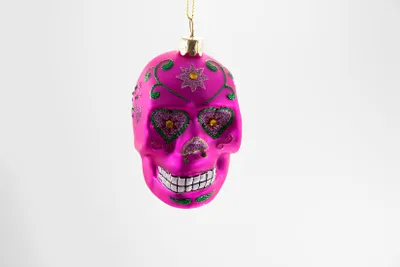 A pink glass skull ornament hangs against a white background.