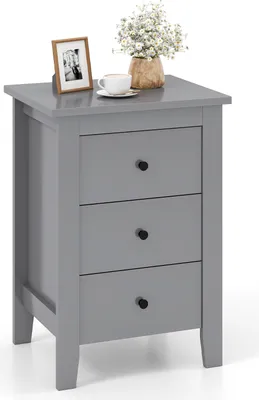 A gray three-drawer nightstand with a framed photo, a cup of coffee, and a vase of flowers on top.