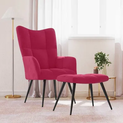 A magenta velvet armchair and matching ottoman are placed on a light pink rug in a room with sheer white curtains and a floor lamp.