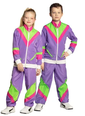 Two children, a boy and a girl, are posing in a studio setting wearing matching 80s-style tracksuits.