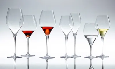 A collection of seven wine glasses of various shapes and sizes, some containing red wine, clear liquid, and white wine, arranged on a reflective surface against a gradient background.