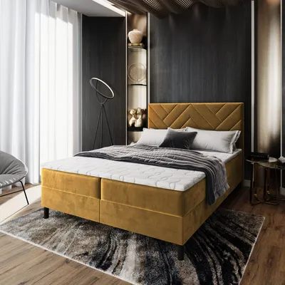 A bedroom scene with a yellow boxspring bed as the main focus, styled with pillows and a blanket. The room has dark walls, a large window with white curtains, and decorative shelves.