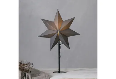 A star-shaped lamp on a stand against a gray wall.