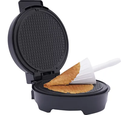 A black waffle maker is open, with two thin, brown waffles placed inside, one being rolled into a cone shape with a white cone-shaped tool.