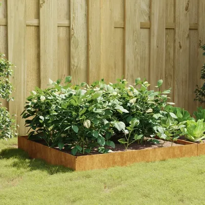 A raised garden bed filled with plants, set against a wooden fence.