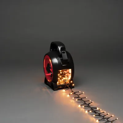 A black reel with red accents holds a string of amber LED lights that are unspooling onto a gray surface.