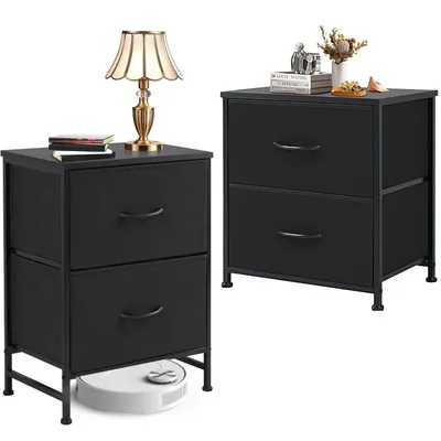 Two black fabric drawer nightstands are shown against a white background. One nightstand has a lamp and books on top, and a robot vacuum cleaner underneath. The other nightstand has books and decorative items on top.