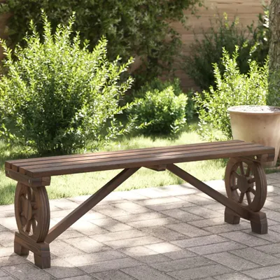 A wooden garden bench with wheel-shaped legs sits on a paved patio, surrounded by lush green bushes and a large terracotta pot.