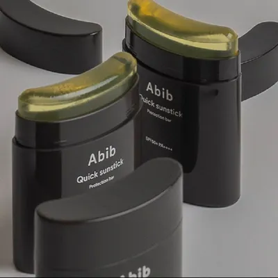 Two black sunstick containers with yellow-green product inside, placed on a light gray surface.