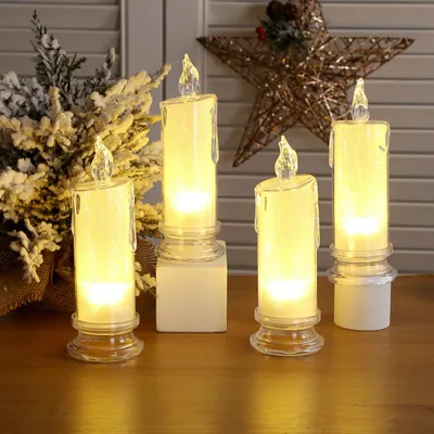 Four LED candles are arranged on a wooden surface, with a snowy branch and a star decoration in the background.