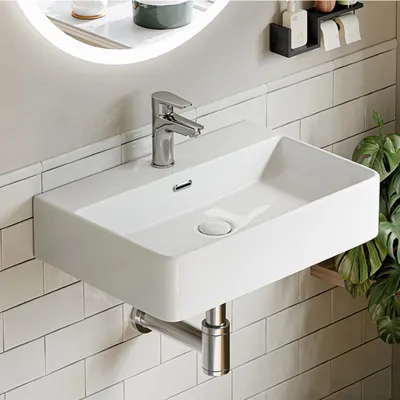 A modern white ceramic wall-mounted sink with a chrome faucet against a tiled wall.