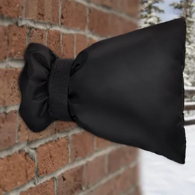 A black insulated cover is attached to an outdoor faucet on a brick wall, with a snowy background.
