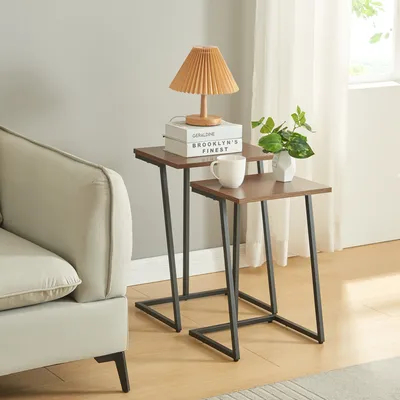 Two nesting side tables with wooden tops and black metal legs are placed next to a sofa in a living room setting.