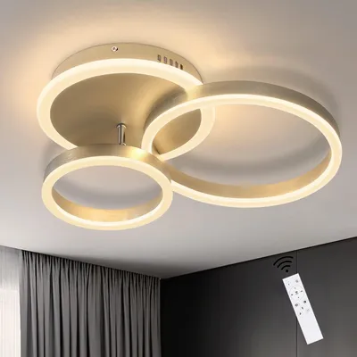 A modern LED ceiling light with three interlocking rings, shown installed on a ceiling. A remote control is visible in the lower right corner.
