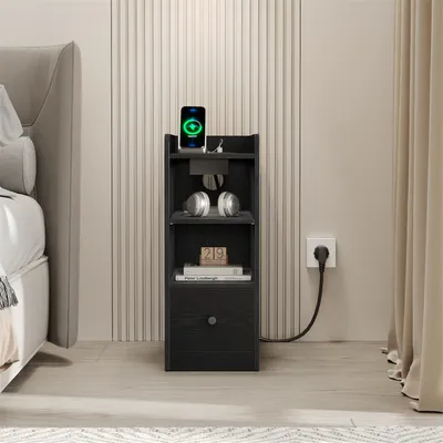 A black nightstand with a phone charging on top, headphones on a shelf, and books on another shelf, placed next to a bed in a bedroom.