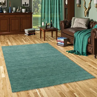 A teal rug is placed on a wooden floor in a living room setting, with a leather sofa and wooden furniture visible.