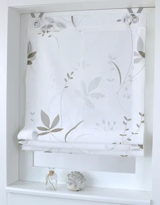 A white Roman blind with a subtle floral pattern is shown hanging in a window frame, with two small decorative items on the windowsill below.