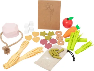 A collection of wooden toy food items and accessories, including a pink block, rope, pasta, vegetables, and shaped food pieces, arranged on a white background.