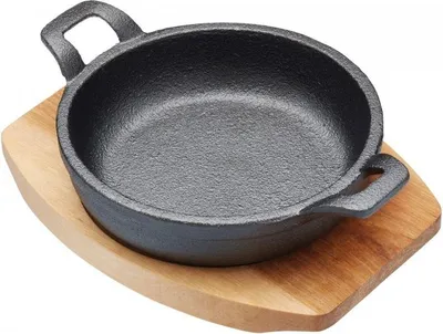 A cast iron mini frying pan with handles sits on a wooden board.