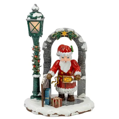 Ein Weihnachtsmann in rotem Anzug steht unter einem steinernen Torbogen neben einem dekorierten Laternenpfahl auf einer schneebedeckten Basis mit Geschenken und einem Schlitten.