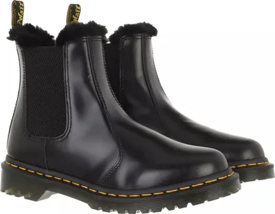A pair of black Dr. Martens Chelsea boots with faux fur lining, shown from a front-side angle against a white background.