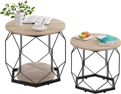 Two round coffee tables with geometric metal bases, one larger with a cushion and plant, the other smaller with fruit and books, on a white background.