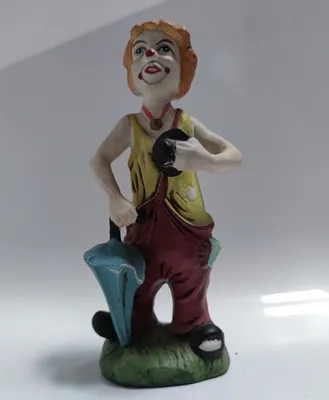 Dies ist eine Keramikfigur eines Clowns, der einen Regenschirm trägt und einen Hut hält. 