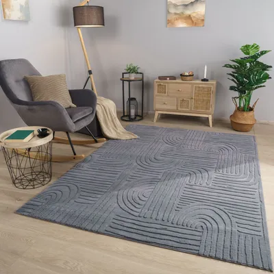 A living room scene with a gray armchair, a floor lamp, a side table, a chest of drawers, a plant, and a rug.