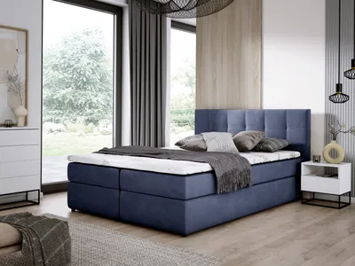 A bedroom scene with a blue boxspring bed as the main focus, set against a large window with greenery outside.